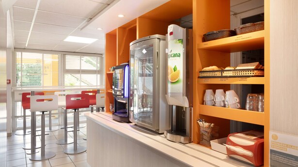 Una estación de bebidas de autoservicio con una máquina de café, un dispensador de jugo y un refrigerador.