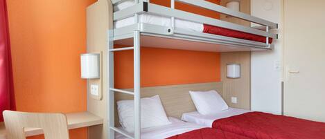 A bunk bed with white bedding and a red blanket, a wooden desk, and a chair with a red seat cushion.