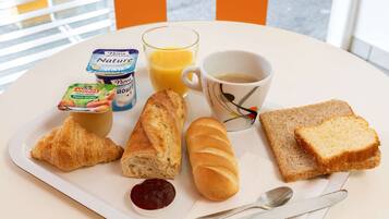 Un plateau de petit-déjeuner avec des croissants, du pain, de la confiture, du jus, du café et du yaourt, posé sur une table blanche.