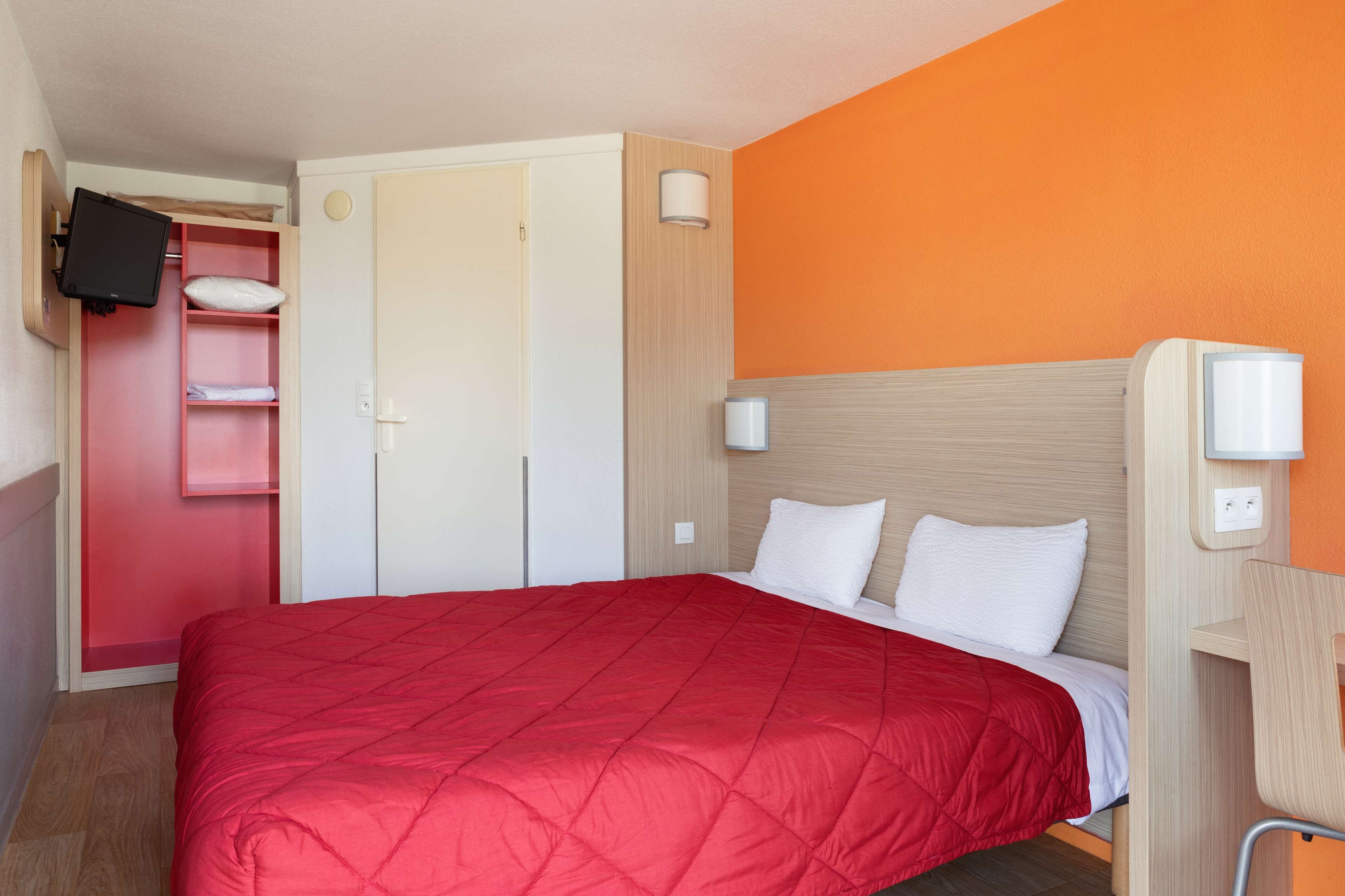 Une chambre d’hôtel comprenant un lit, un téléviseur fixé au mur, une armoire et une table de chevet avec une lampe.