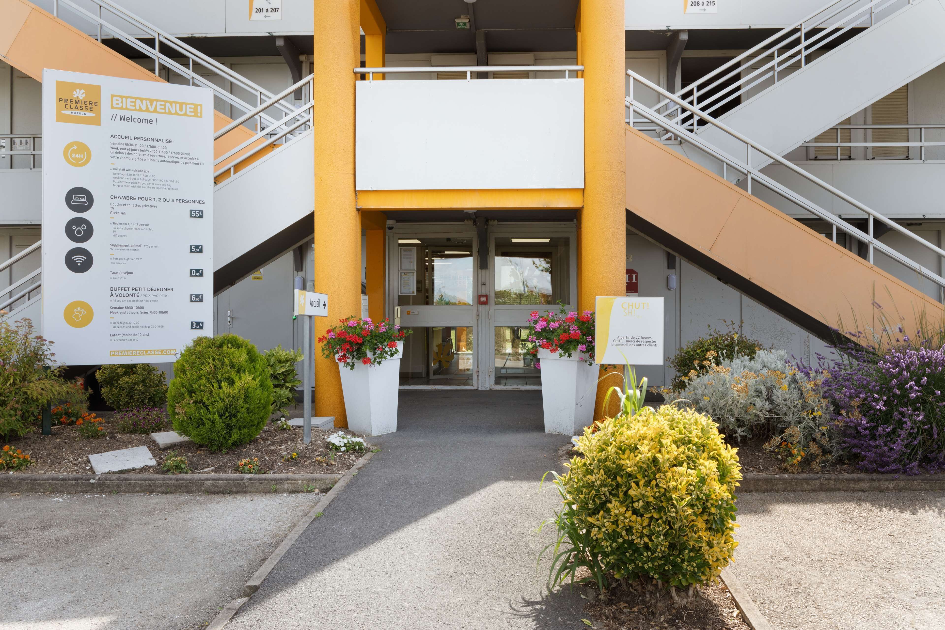 Entrada de hotel con letrero, escaleras y plantas en macetas.