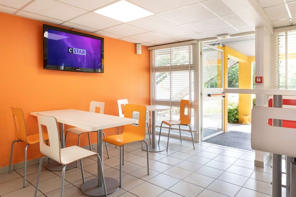 A brightly lit indoor space with orange walls, white tables and chairs, and a television displaying 'C STAR'.