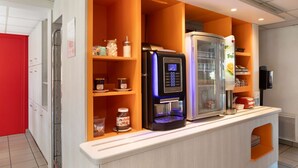 Una estación de bebidas de autoservicio con una cafetera, refrigerador y estantes llenos de condimentos y bocadillos.