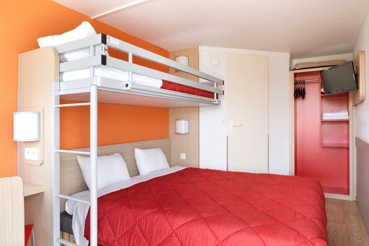 A bunk bed with a red quilt, a wardrobe, a television, and a mirror.