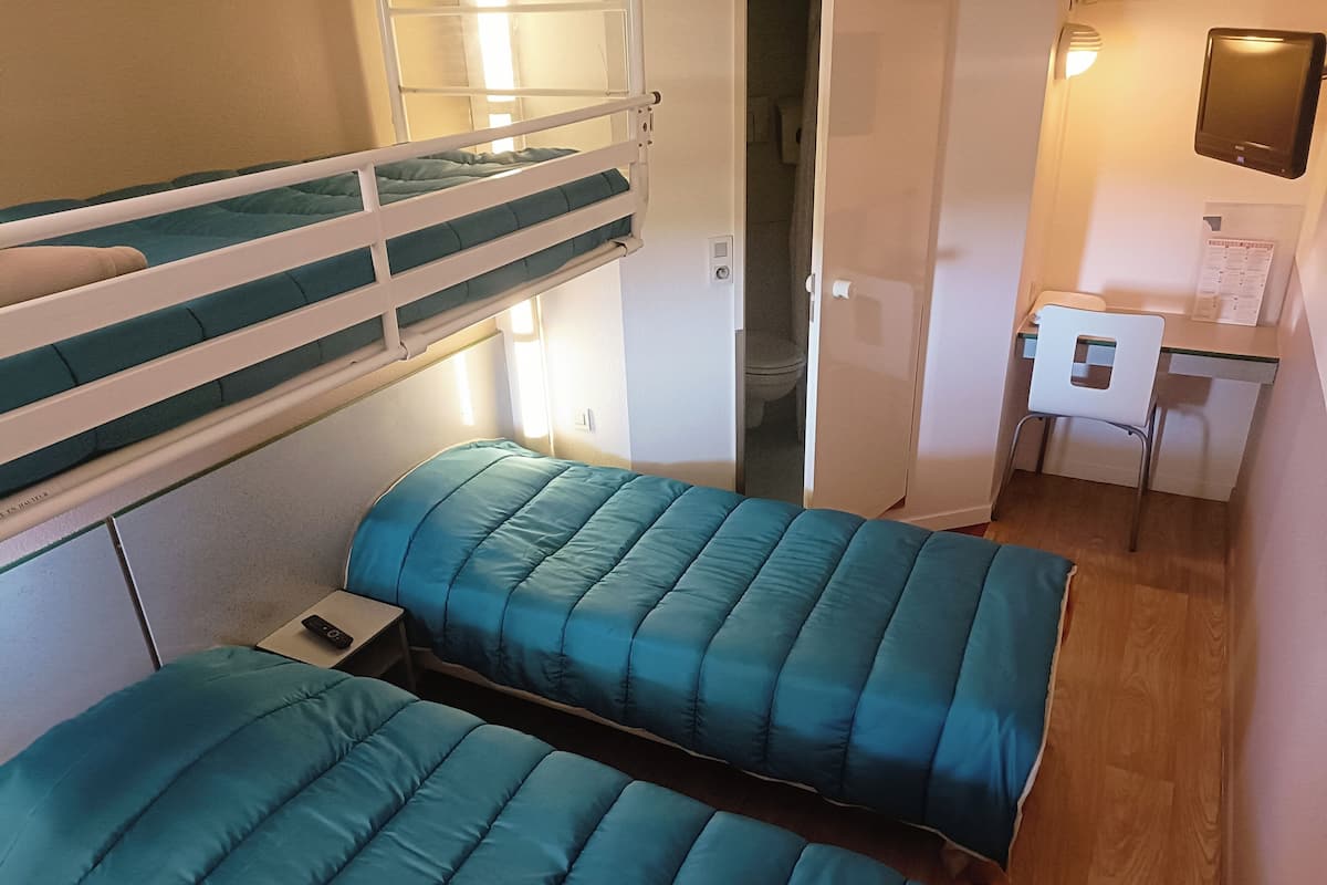 Une chambre avec un lit superposé, un bureau et une chaise, une petite table et un téléviseur fixé au mur.
