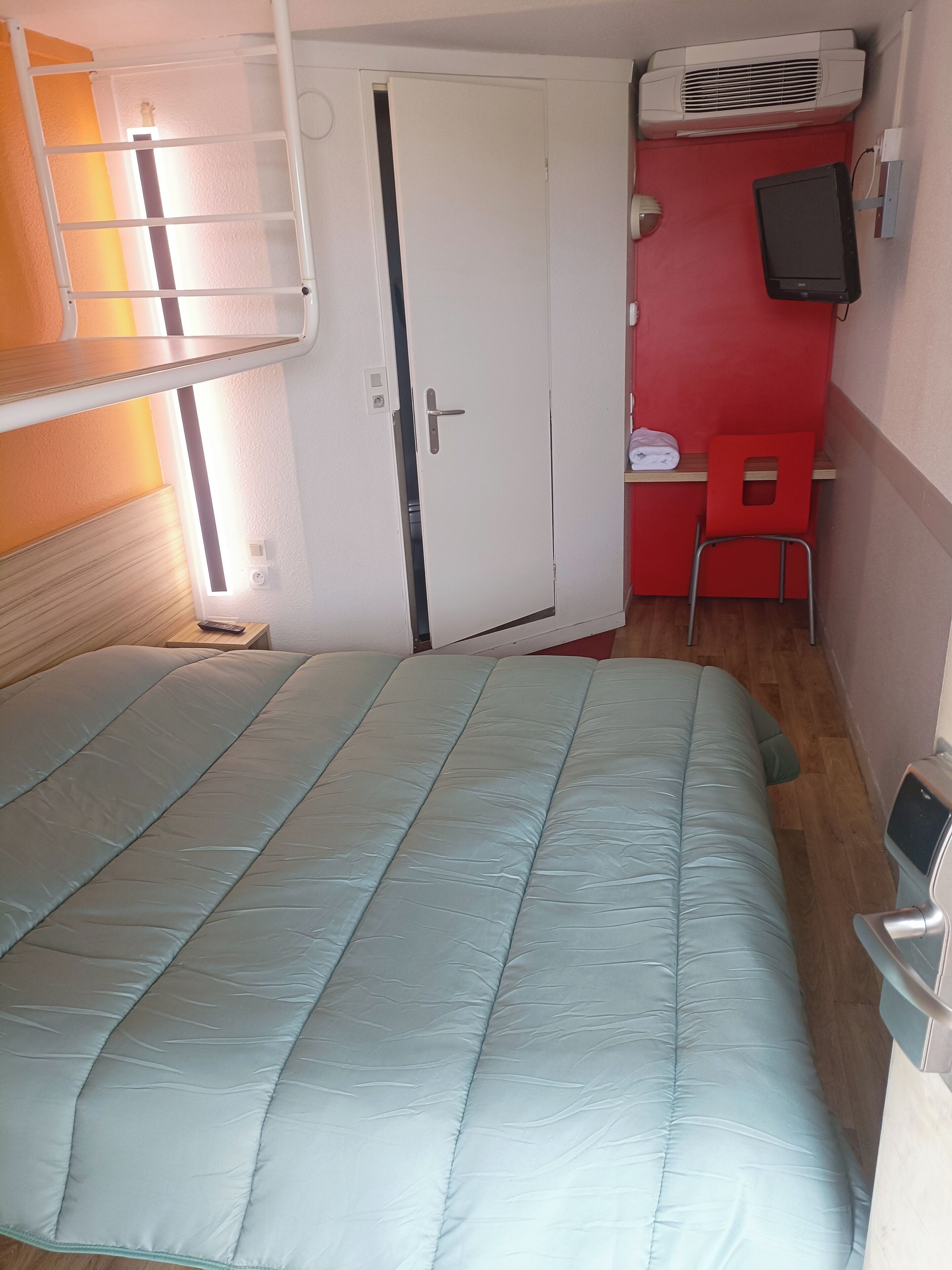 A compact room with a bunk bed, a desk with a chair, a television, and a red wall.