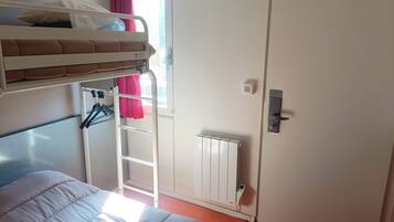 A bunk bed with a white headboard, a radiator, a door with a handle, and a window with a red curtain.
