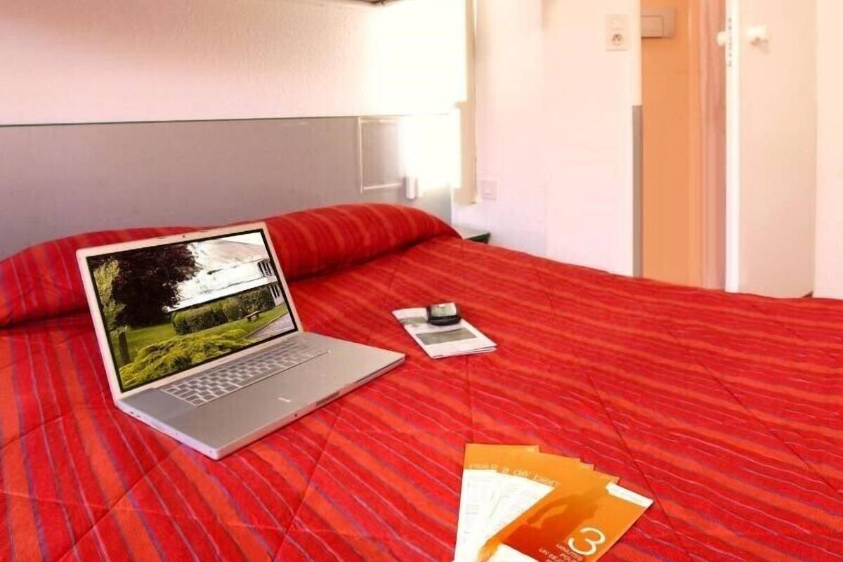 Une chambre d’hôtel avec un lit, un ordinateur portable, un téléphone portable et quelques brochures posées sur le lit.