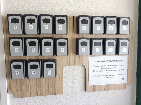 A wall-mounted luggage storage system with numbered compartments, a sign with instructions for late arrivals, and a wooden panel. - Classic Hôtel Reims Est Taissy (Taissy)