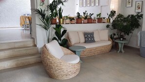 A living room with a wicker sofa, a small round table, and a variety of potted plants. - Helios Splendid (Corfu)