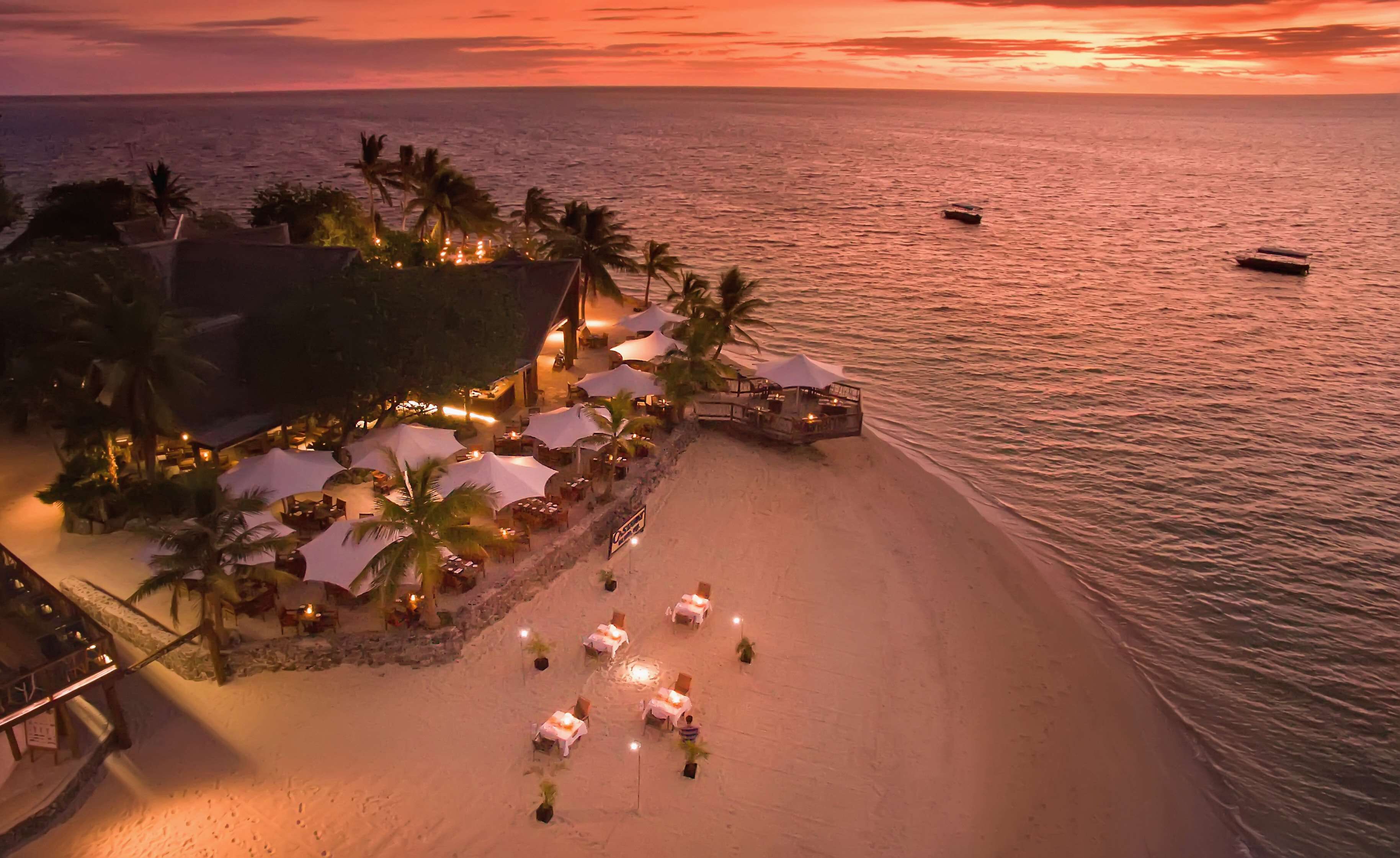 A beachfront resort with outdoor seating and umbrellas, a pool area, and a view of the ocean.