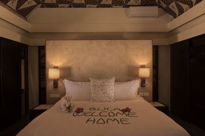 A hotel room with a large bed, two bedside lamps, and a ceiling with a geometric pattern.