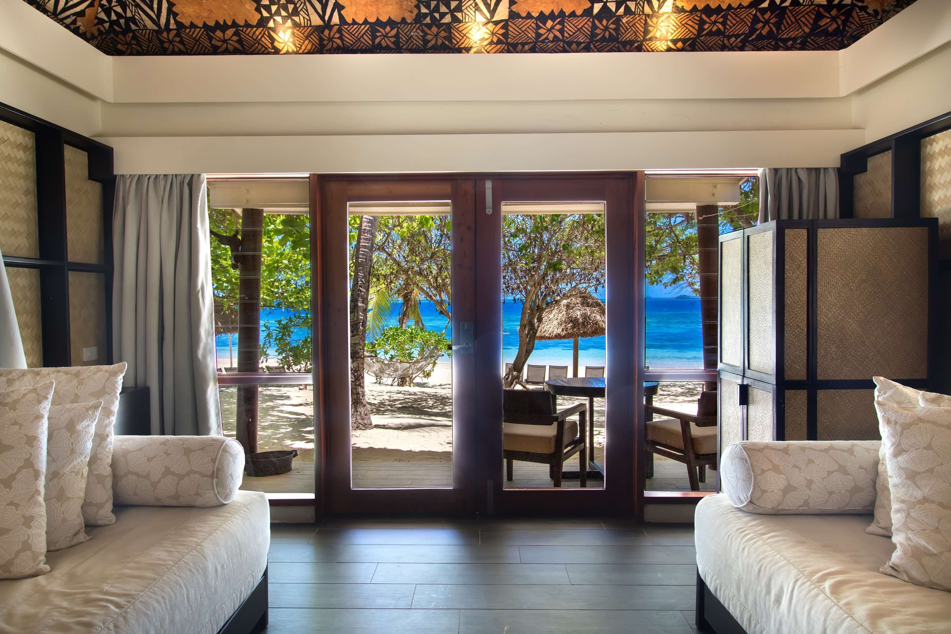 A room with a view of a beach, a sofa, and a table with chairs.