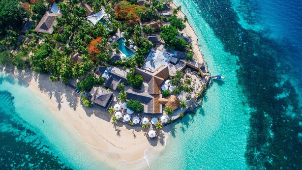 An aerial view of a tropical island resort with a central building surrounded by palm trees and a beach. - Castaway Island, Fiji (Castaway Island)