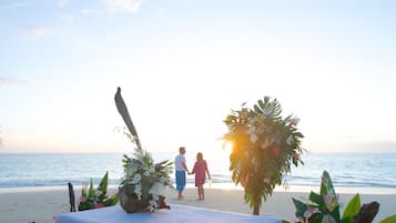Walk hand in hand along the serene shoreline, surrounded by tropical plants and a beautiful ocean view.