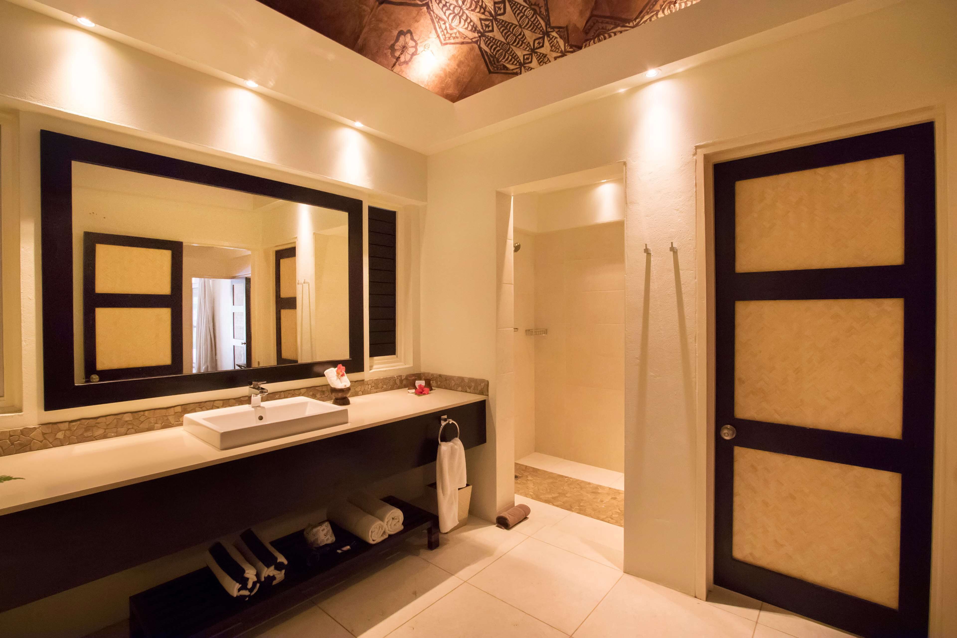 A modern bathroom with a large mirror, a sink, a shower, and a door with a geometric pattern.