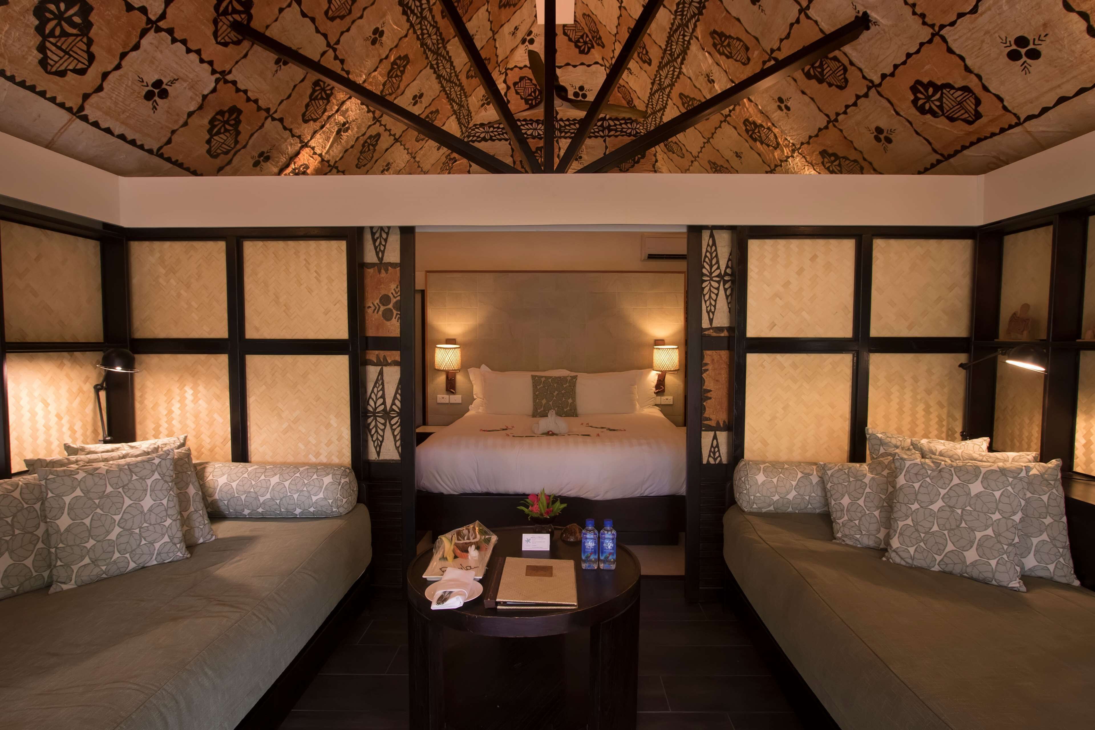 A hotel room with a large bed, two sofas, a small table with amenities, and patterned walls.