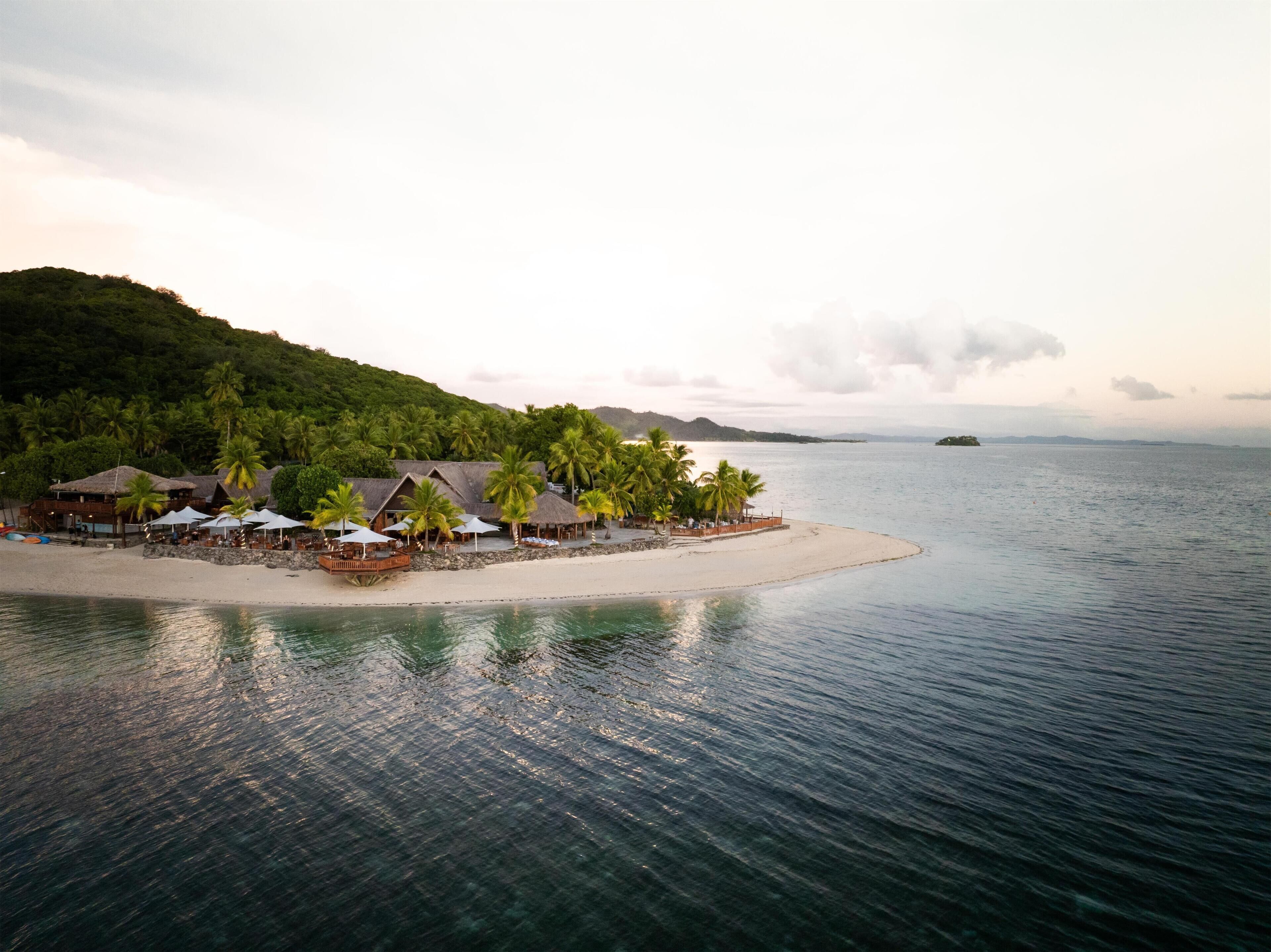 A beach resort with thatched-roof buildings, palm trees, and a sandy beach.