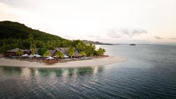 A beach resort with thatched-roof buildings, palm trees, and a sandy beach.