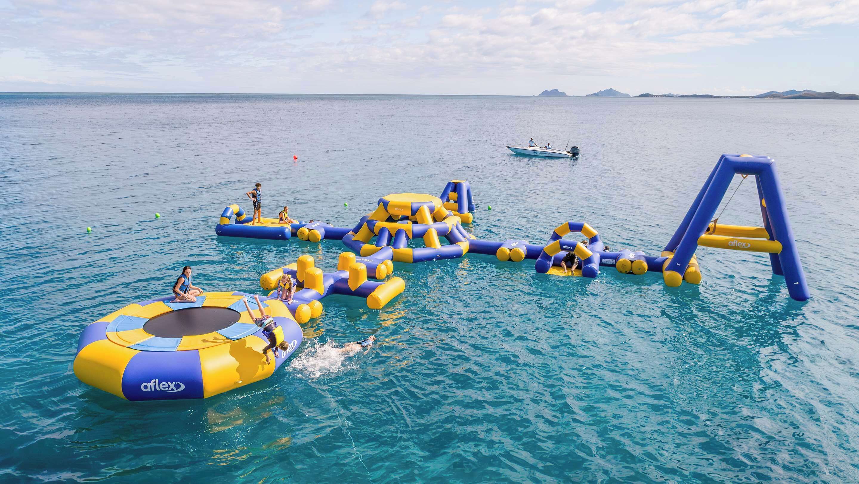 Um parque aquático inflável com diversas estruturas de recreação e um barco ao fundo.
