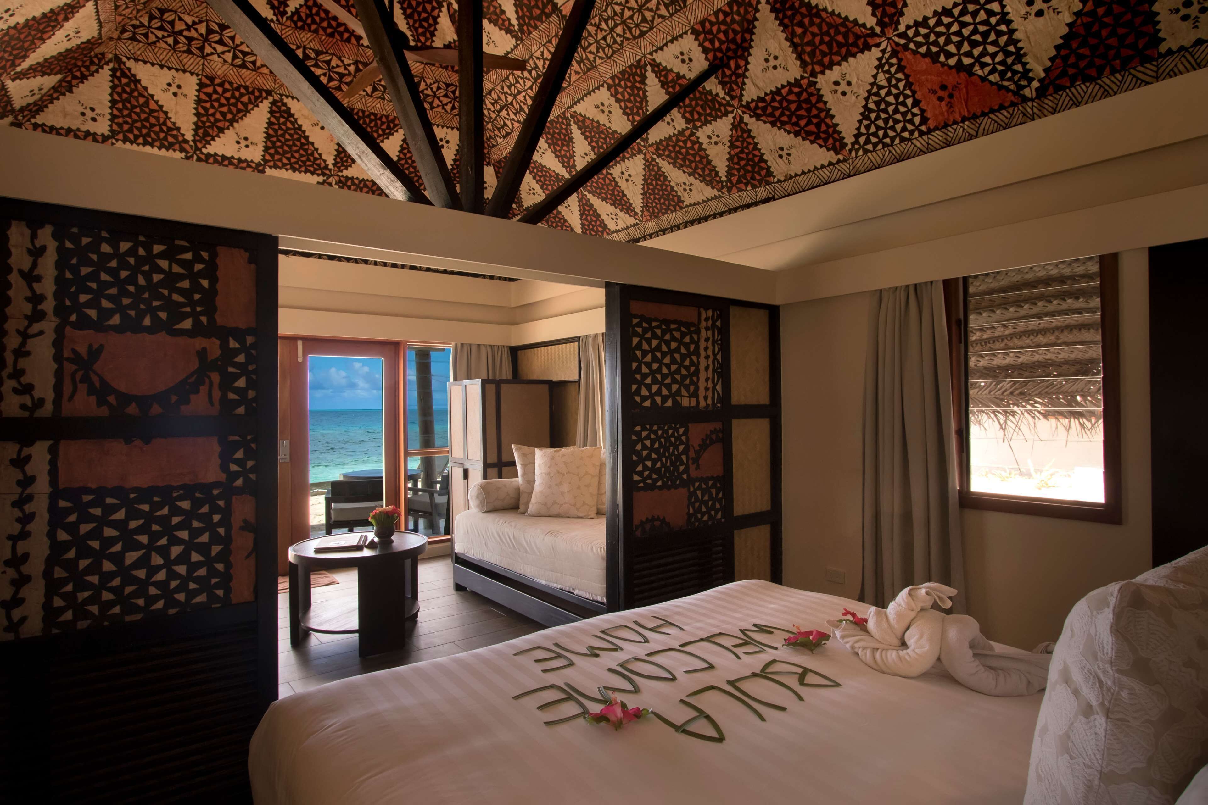 Een hotelkamer met een bed, een bureau, uitzicht op zee en behang met een patroon.
