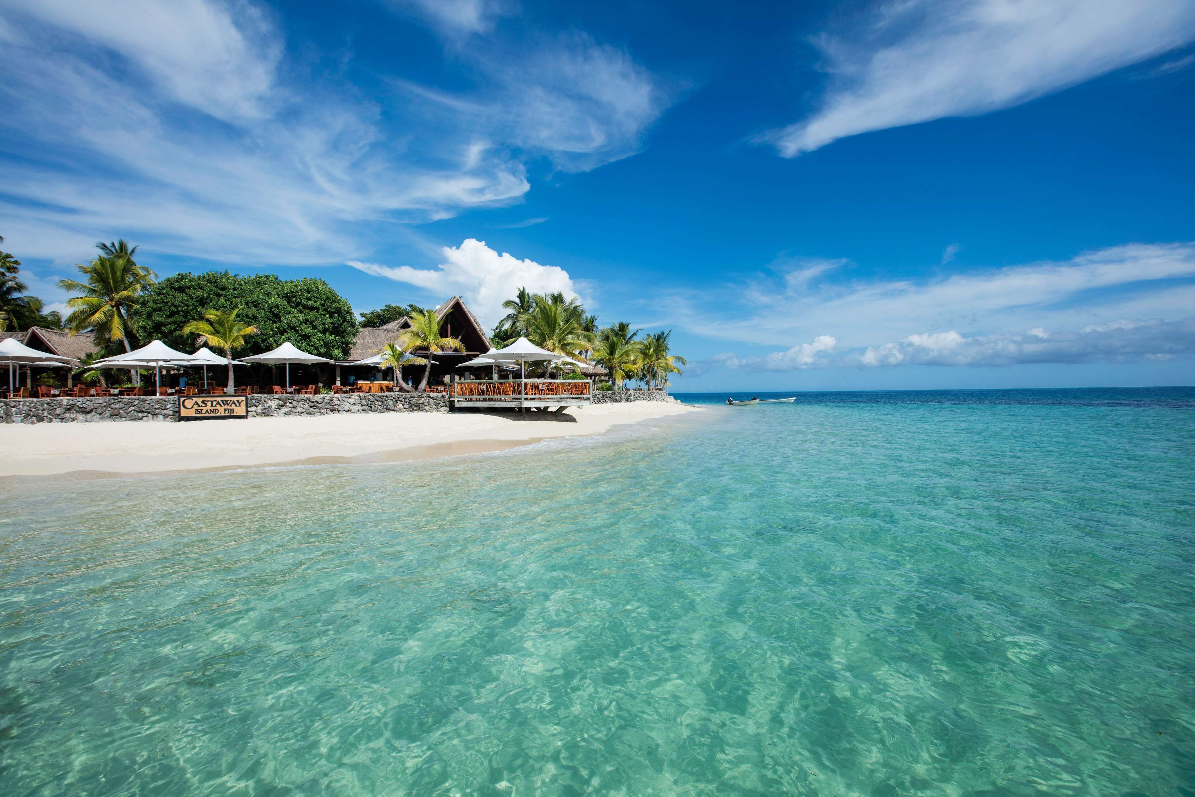 A beach resort with clear turquoise water, white sand, and overwater bungalows with umbrellas.