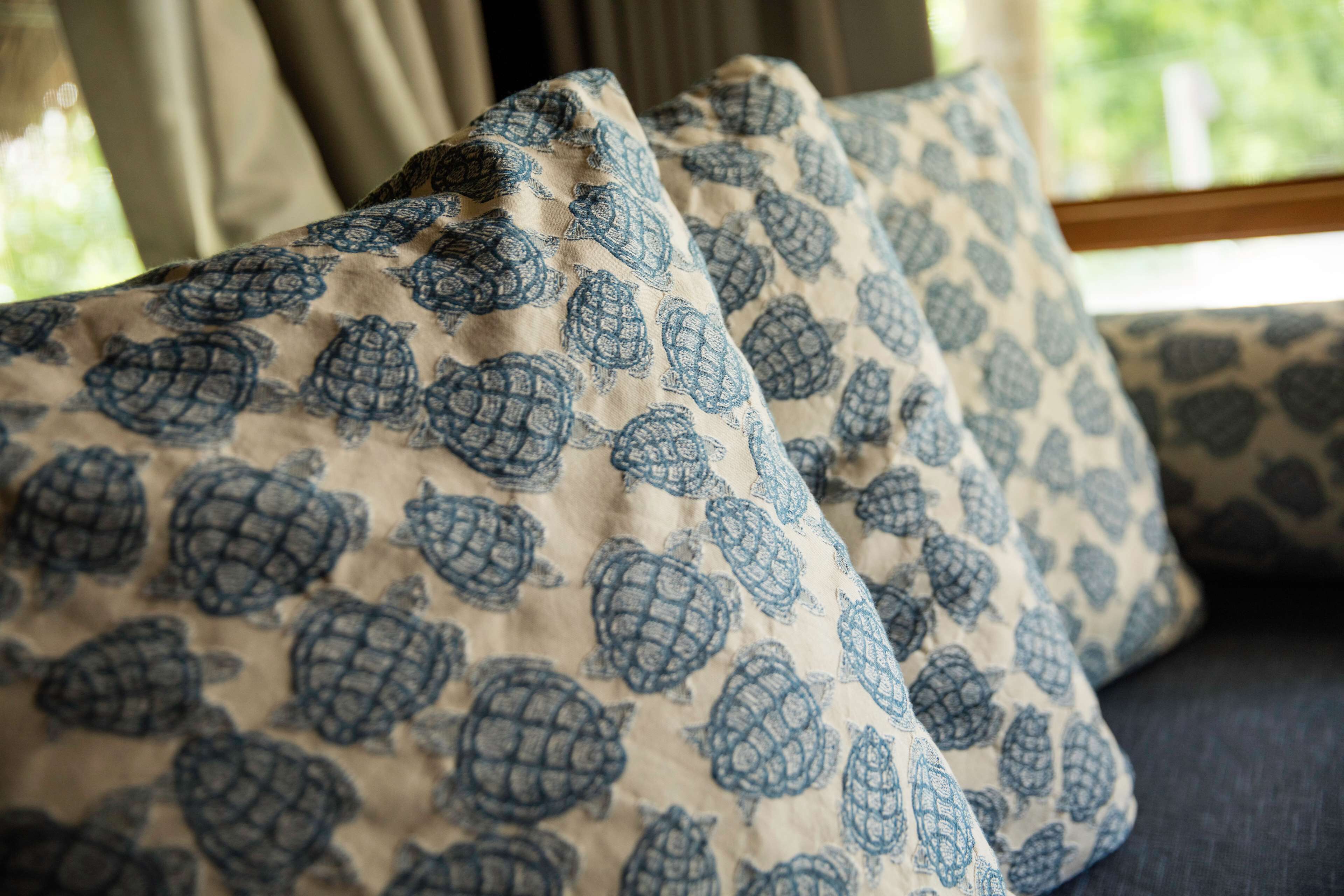 A close-up of a patterned pillow with a turtle design, placed on a sofa.