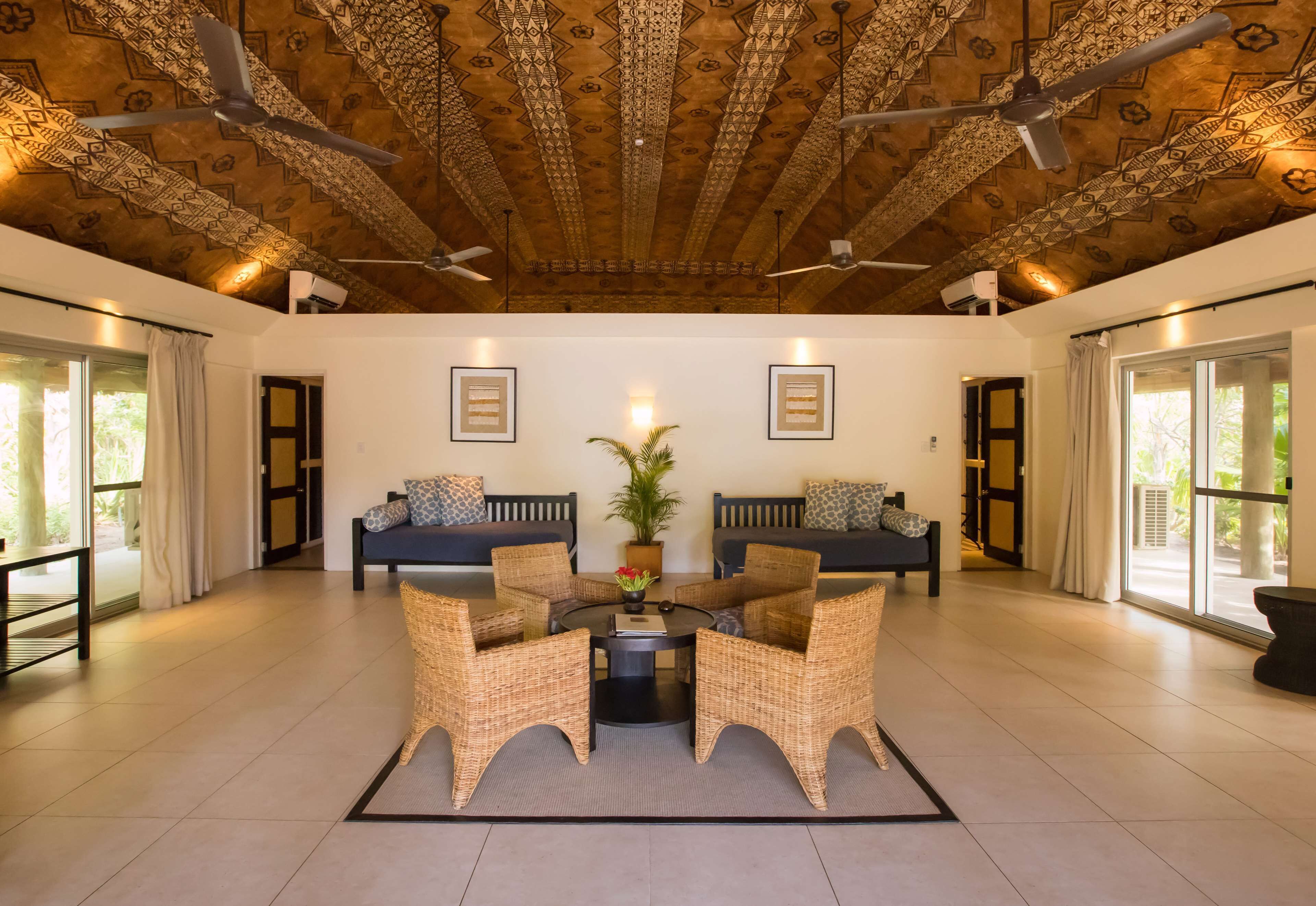 A spacious room with a high ceiling, patterned ceiling, two sofas, a round table, and a potted plant.