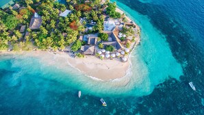 An aerial view of a tropical island resort with a beach, thatched-roof buildings, and clear turquoise waters. - Castaway Island, Fiji (Castaway Island)