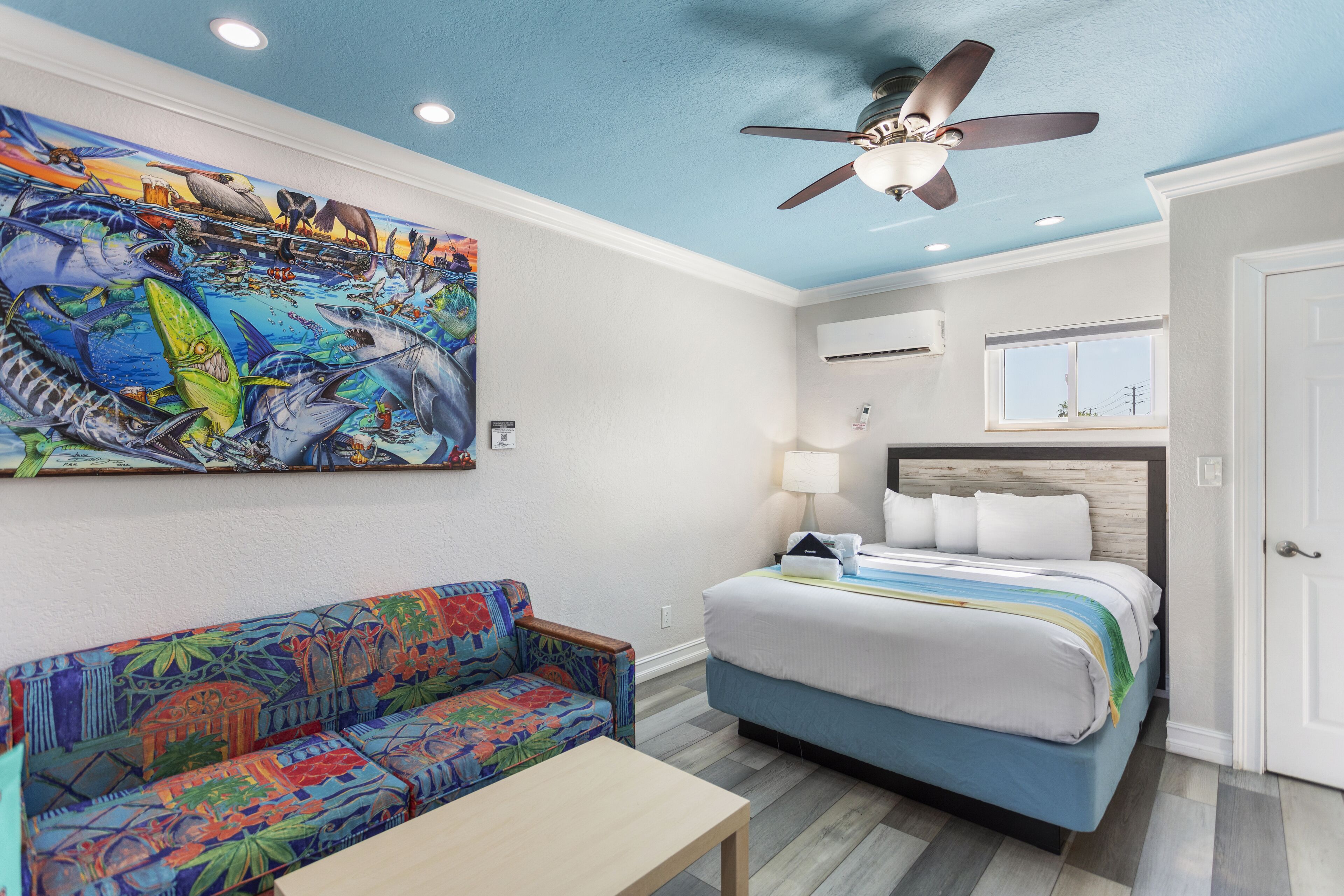 A room with a bed, a colorful sofa, a ceiling fan, and a mural on the wall.
