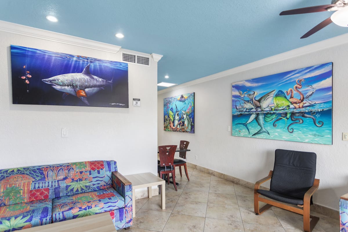 A room with a colorful sofa, a dining table with chairs, and two paintings depicting marine life.