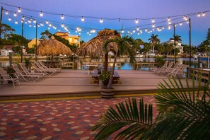 A poolside area with lounge chairs, a thatched-roof structure, and string lights. - Bay Palms Waterfront Resort - Hotel and Marina (St. Pete Beach)
