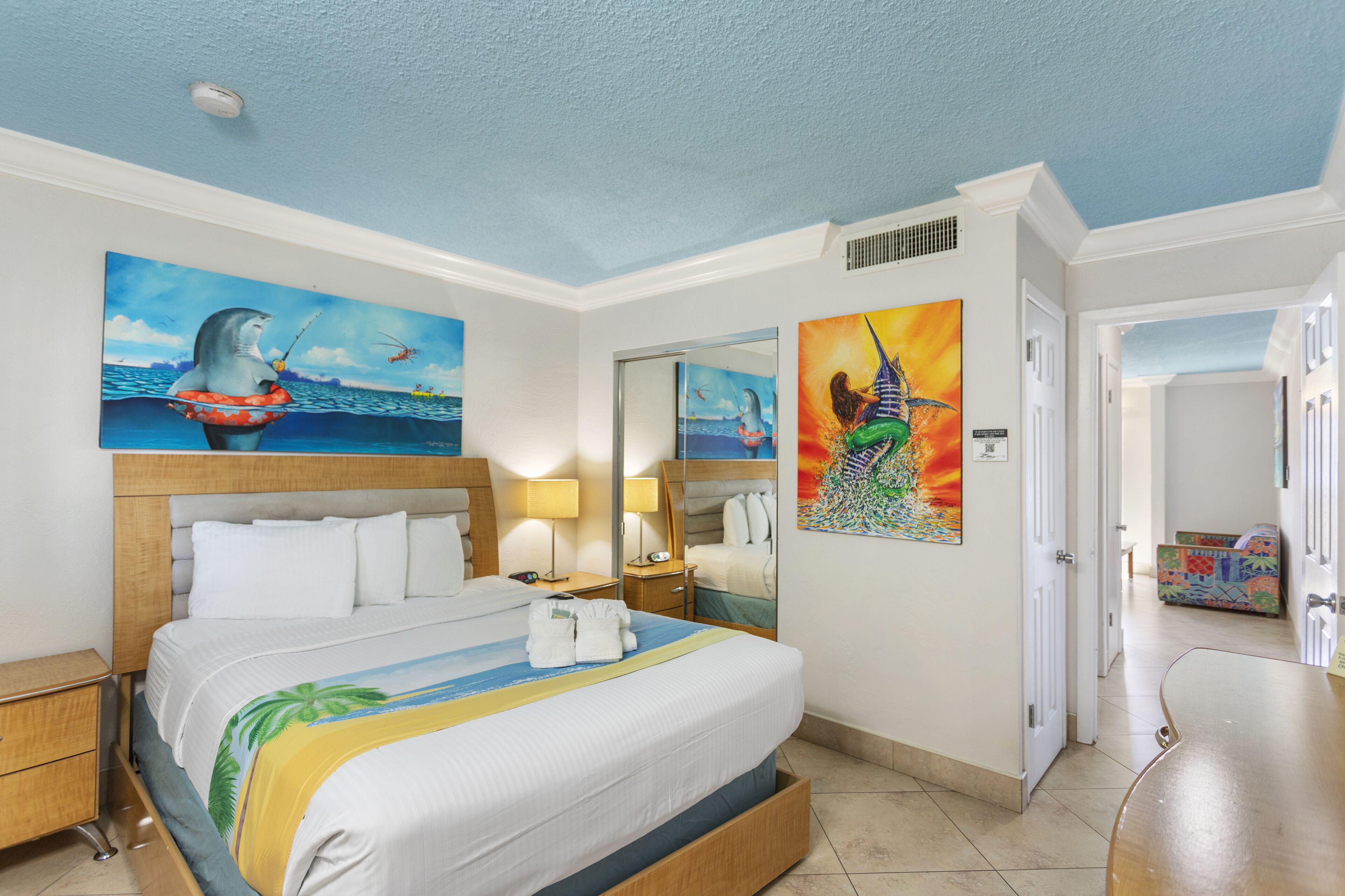 Habitación de hotel con una cama grande, dos mesitas de noche con lámparas, un espejo y obras de arte en las paredes.