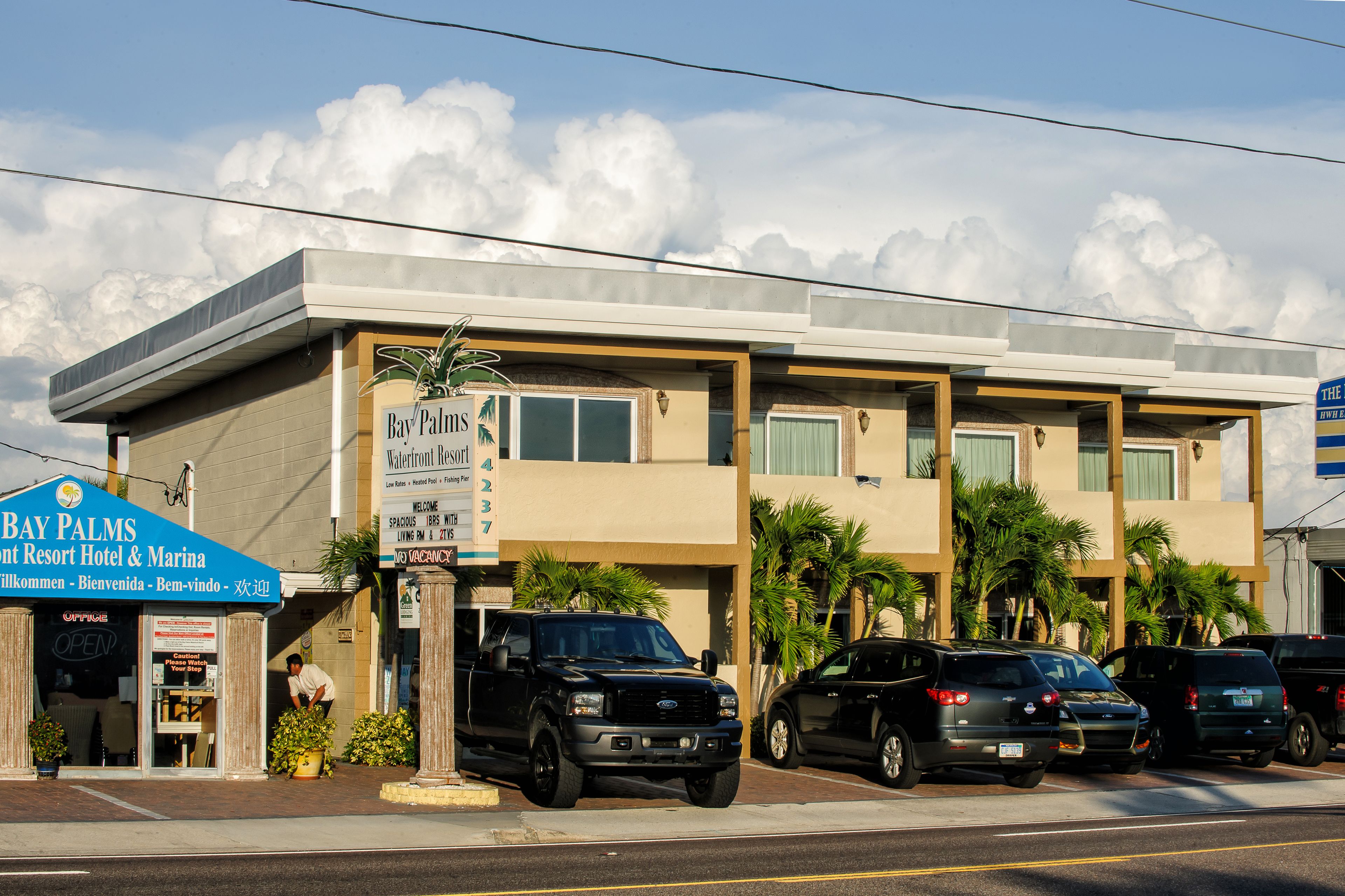 A hotel with a sign for Bay Palms Resort Hotel & Marina. There are parked cars in front, and palm trees are visible.
