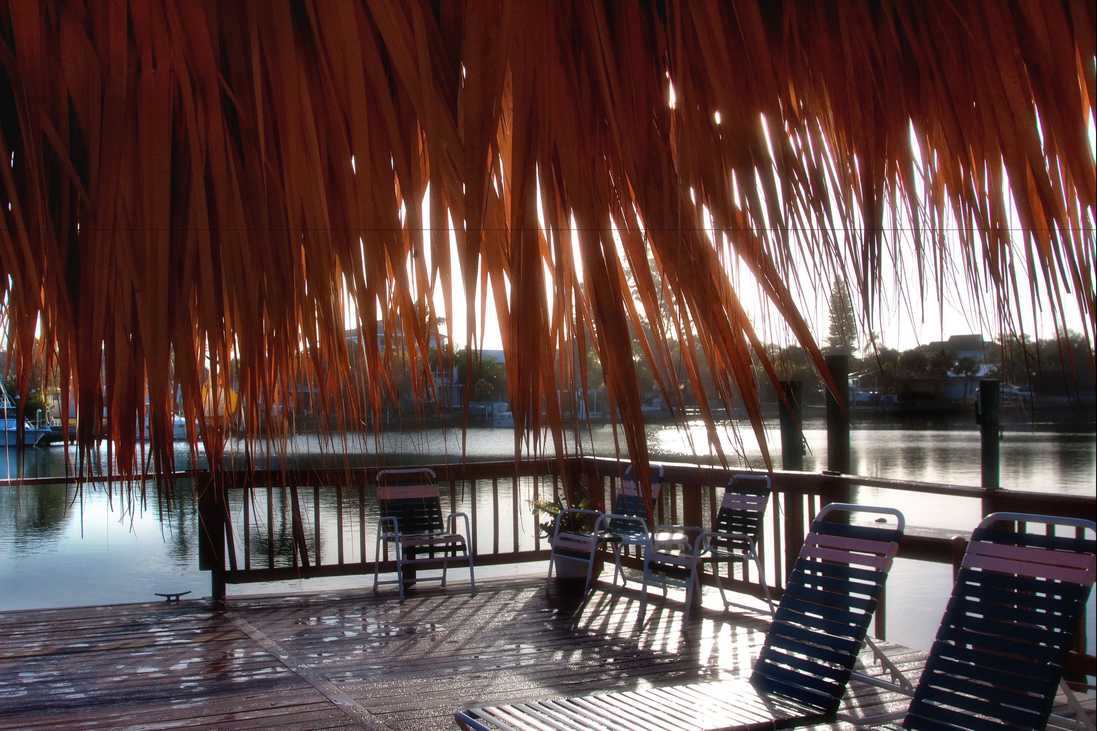 A covered outdoor seating area with chairs and a view of a calm body of water.