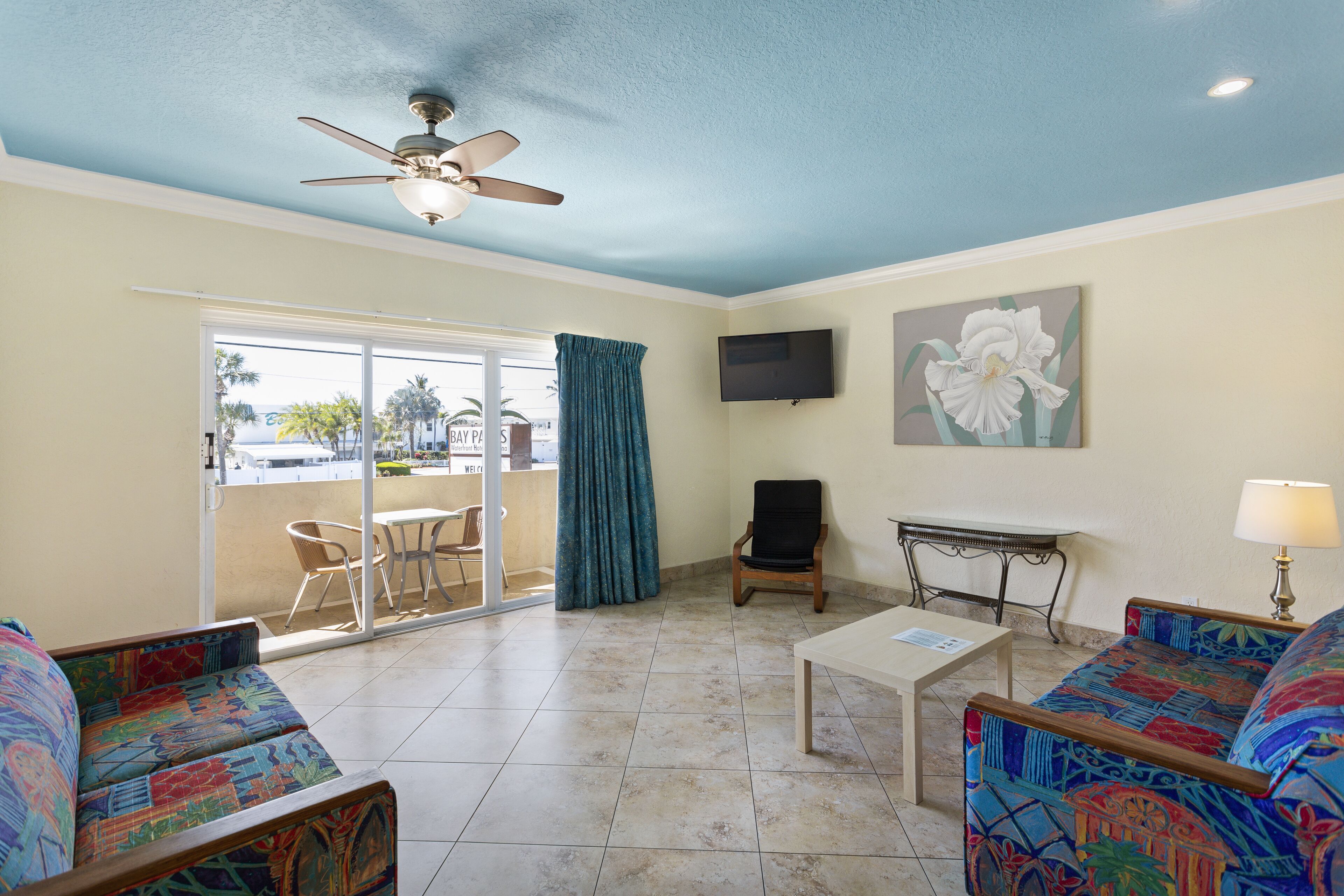 A living room with a ceiling fan, a TV, a sofa, a coffee table, and a view of the outside.