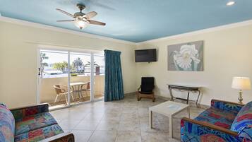A living room with a ceiling fan, a TV, a sofa, a coffee table, and a view of the outside.