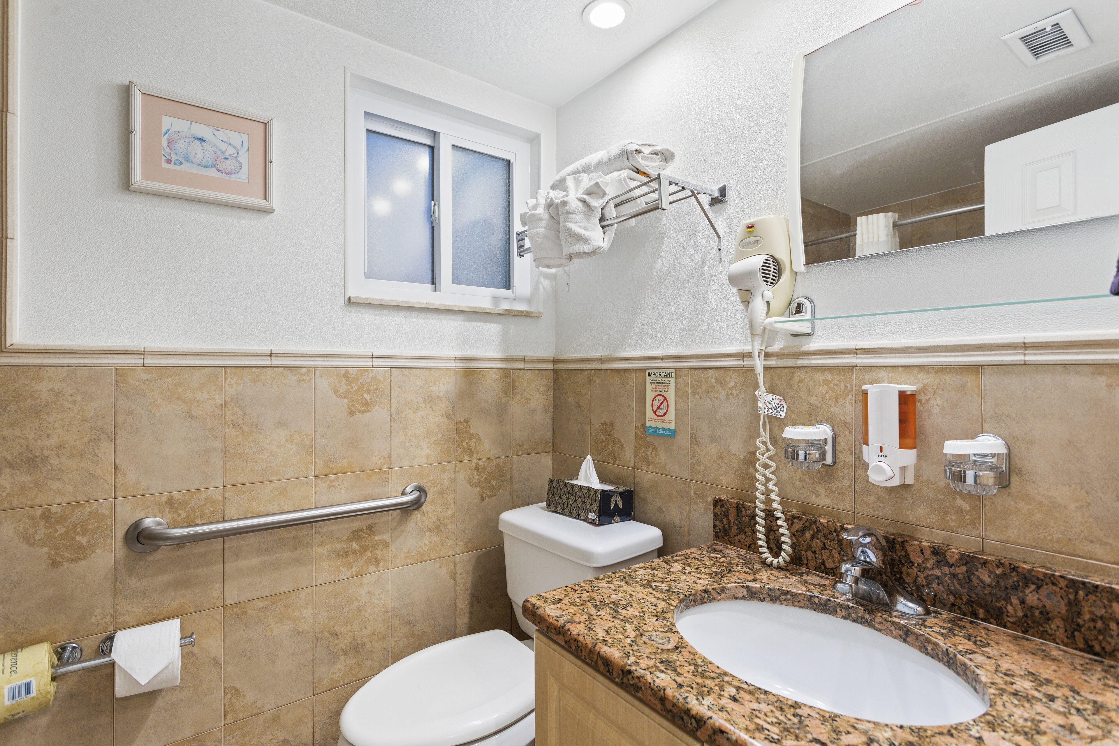 Un baño con inodoro, lavamanos, toallero y ventana.