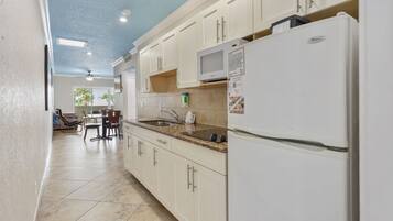 A kitchen with white cabinets, a white refrigerator, a microwave, and a sink. There is a dining area with a table and chairs in the background.