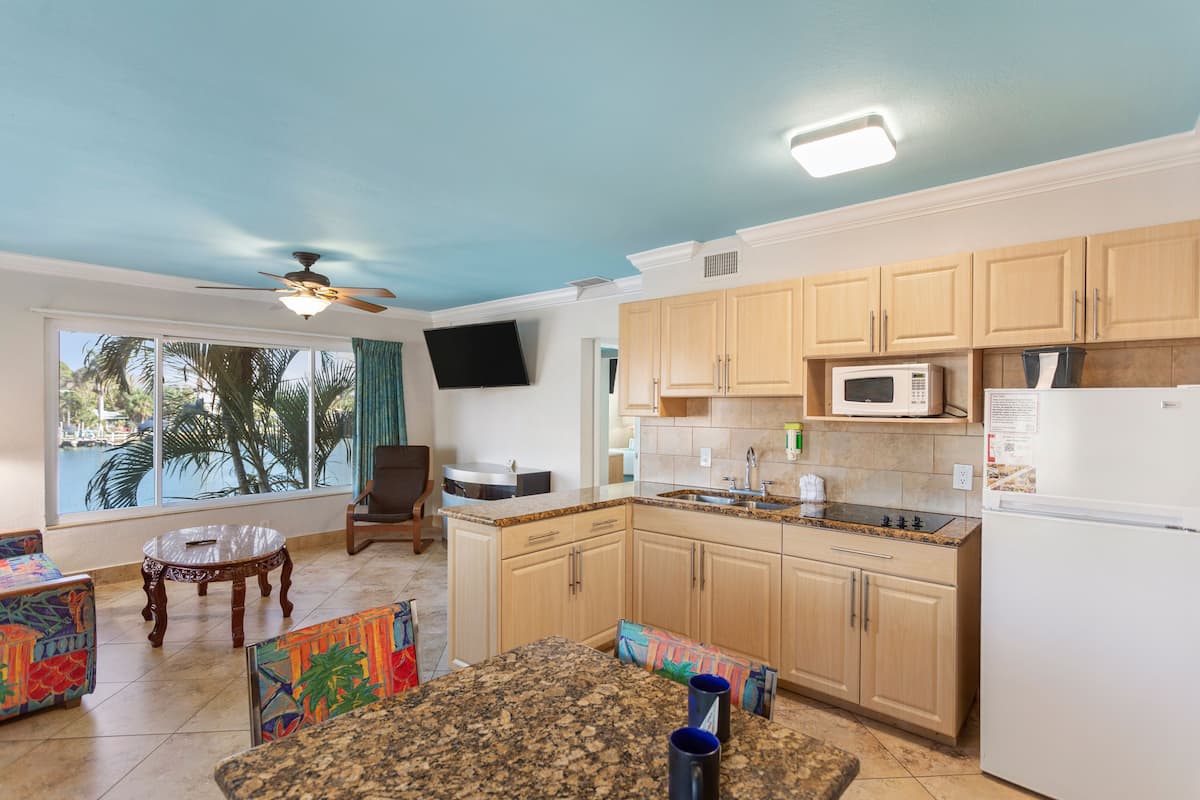 A kitchen with wooden cabinets, a microwave, and a refrigerator. There is a dining table with chairs and a ceiling fan.