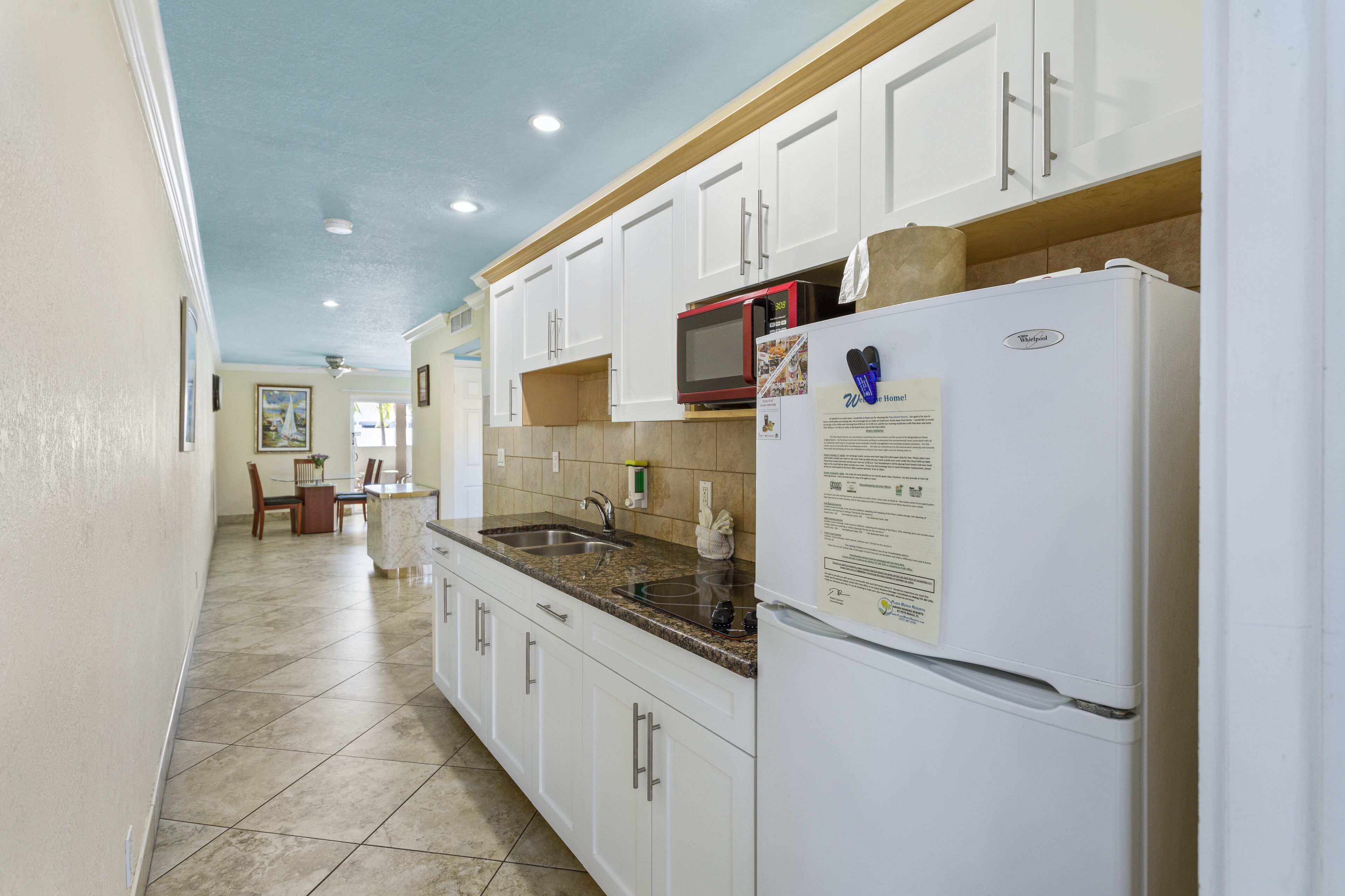 A kitchen with white cabinets, a granite countertop, a refrigerator, and a microwave.