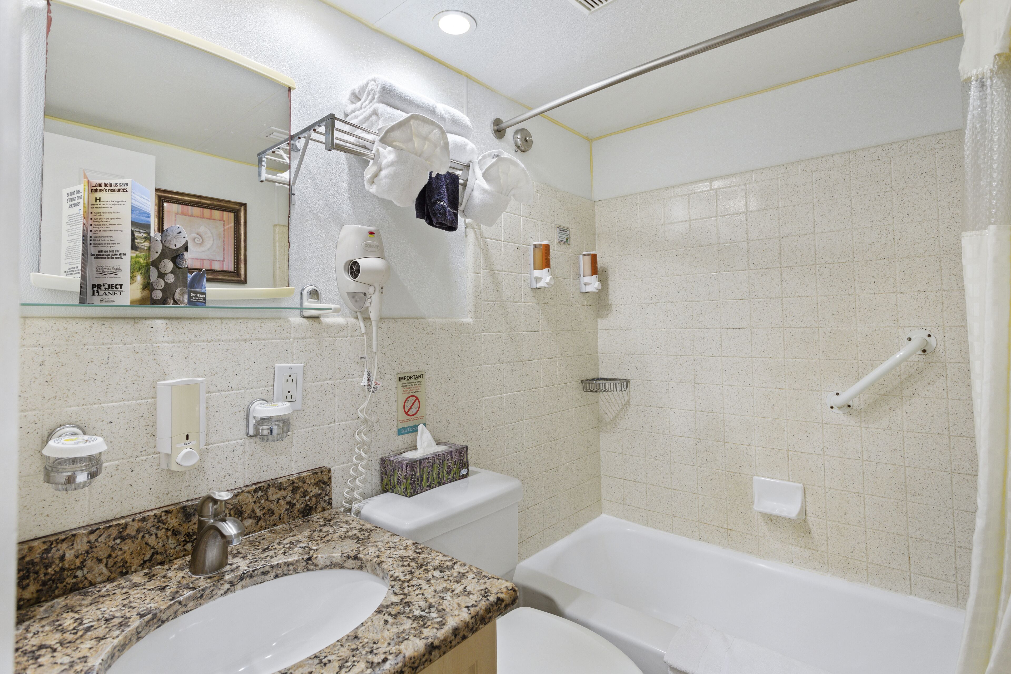 Un baño con encimera de granito, dos lavamanos, inodoro, bañera y ducha con mampara de vidrio.