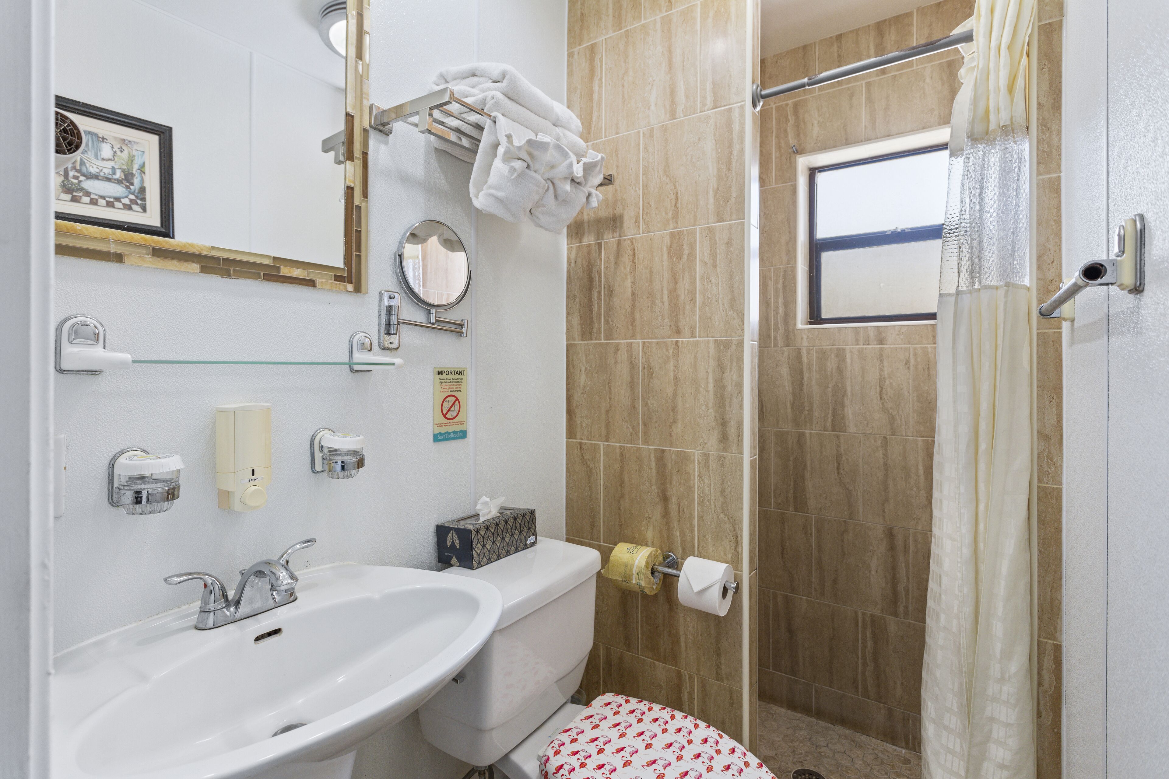 Un bagno con lavandino, wc e doccia. Asciugamani appesi a un porta-asciugamani, un quadro appeso al muro e una finestra.