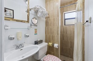 Un bagno con lavandino, wc e doccia. Asciugamani appesi a un porta-asciugamani, un quadro appeso al muro e una finestra.