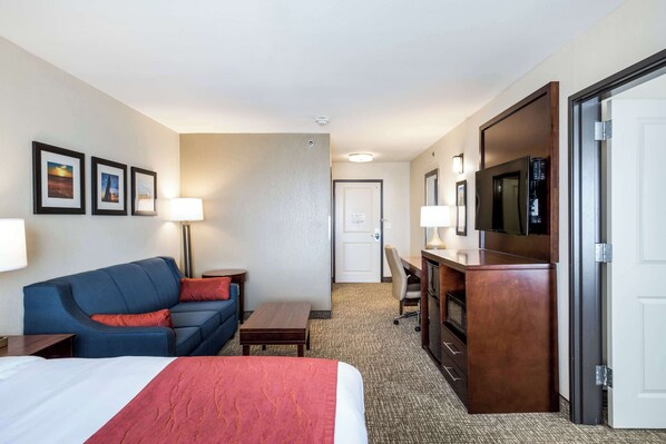A hotel room with a bed, a blue sofa, a desk, a TV, and a door. - Comfort Inn Bonner Springs Kansas City (Bonner Springs)
