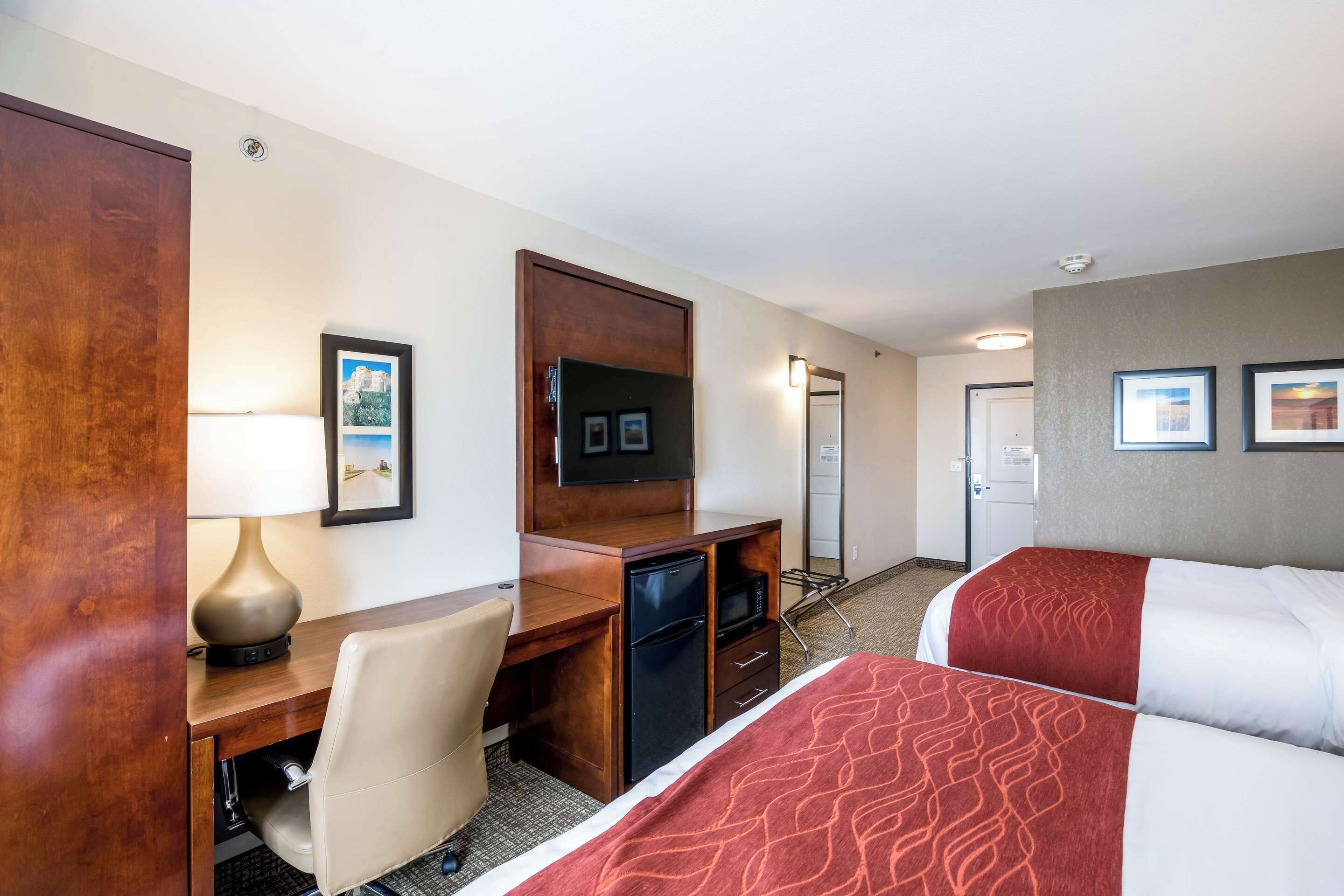 Habitación de hotel con escritorio, silla, cama, televisor y un refrigerador pequeño.