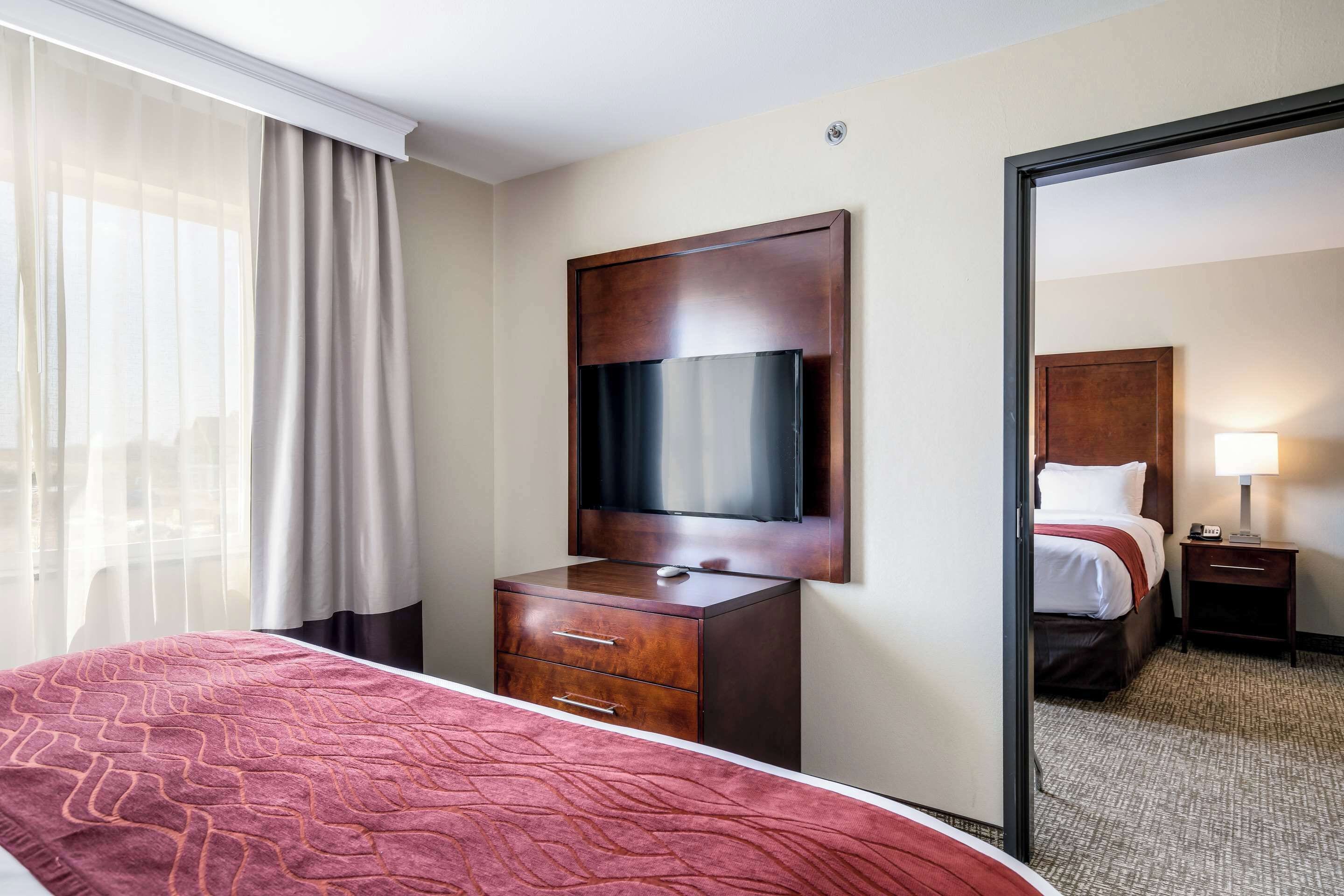 Ein Hotelzimmer mit Bett, einem Holzschrank, einem Flachbildfernseher, einem Nachttisch mit Lampe und einem großen Spiegel.
