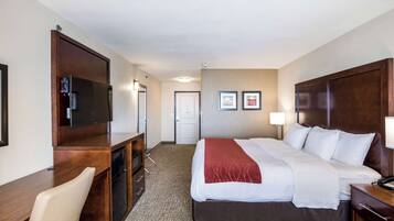 Una habitación de hotel con cama, escritorio, silla, televisor y una puerta.