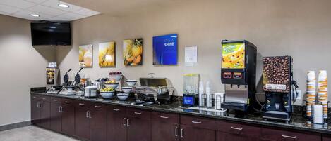 Zona de recepción de hotel con mostrador, máquinas de café y un televisor montado en la pared.
