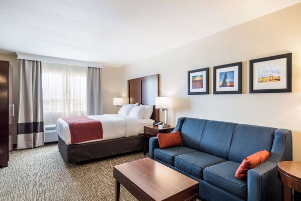 A hotel room with a bed, a sofa, a coffee table, a desk with a lamp, and framed pictures on the wall.